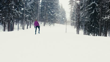 WIDE-TRACKING-Back-view-of-young-adult-Caucasian-female-athlete-practicing-cross-country-skiing-on-a-scenic-forest-trail.-4K-UHD-60-FPS-SLO-MO